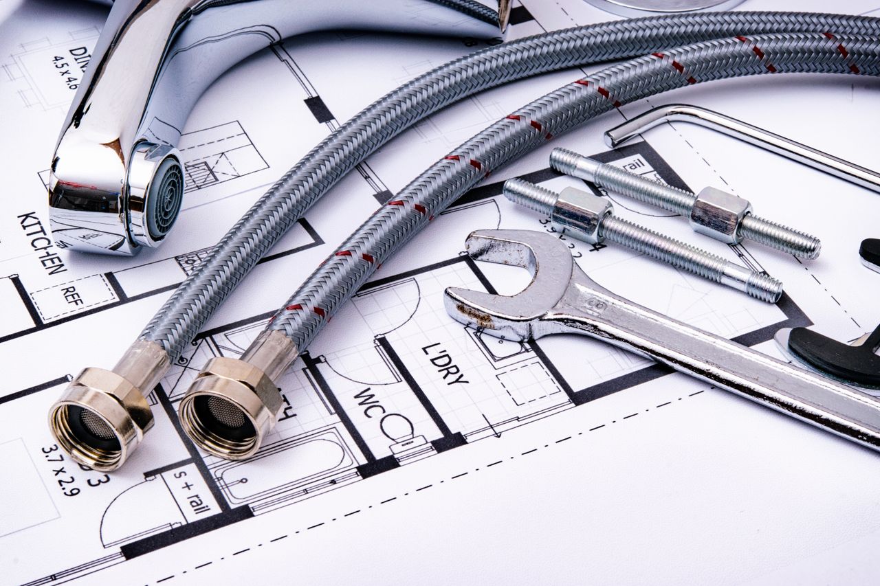 heros-img Close-up of plumbing tools and faucet on top of an architectural blueprint, perfect for hardware and construction themes.
