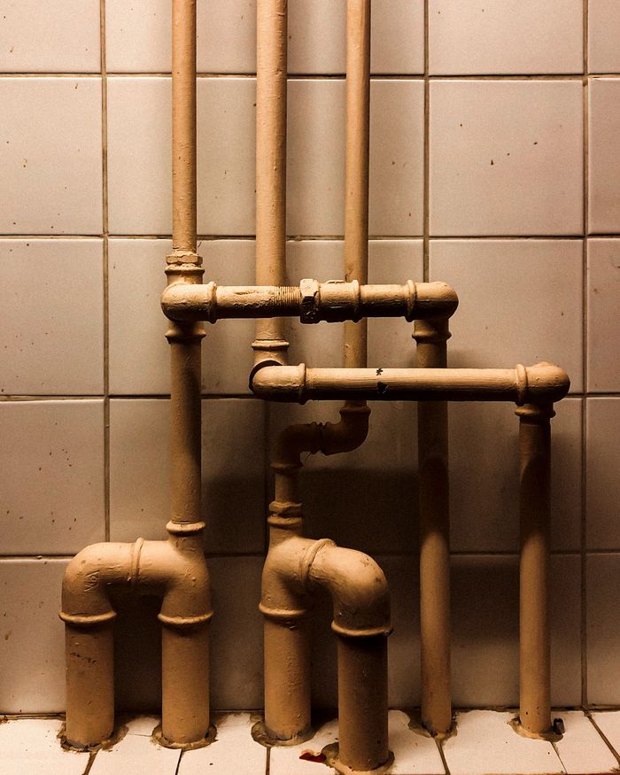 about-us-01 An artistic capture of vertical industrial pipes against a tiled wall, showcasing geometry.